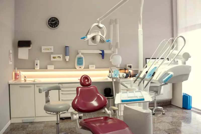 A clean dental room with a maroon dental chair, sink and instruments