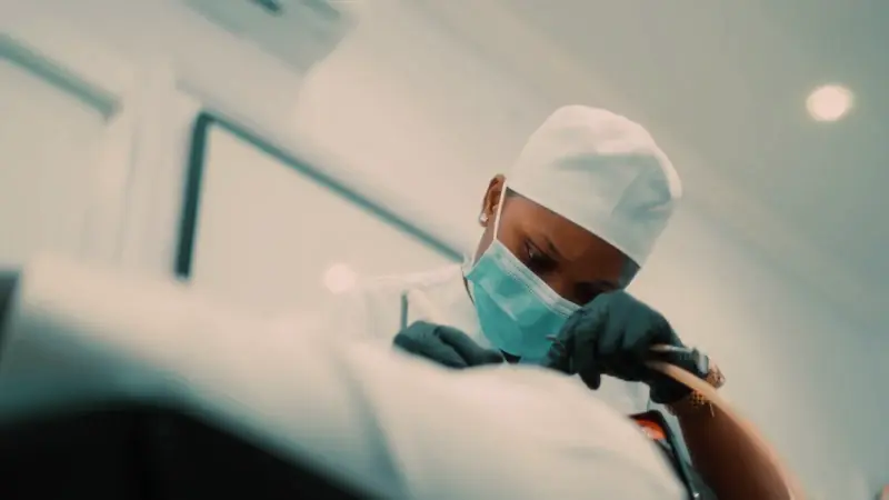 A dentist in a mask and cap leaning over a patient during a procedure